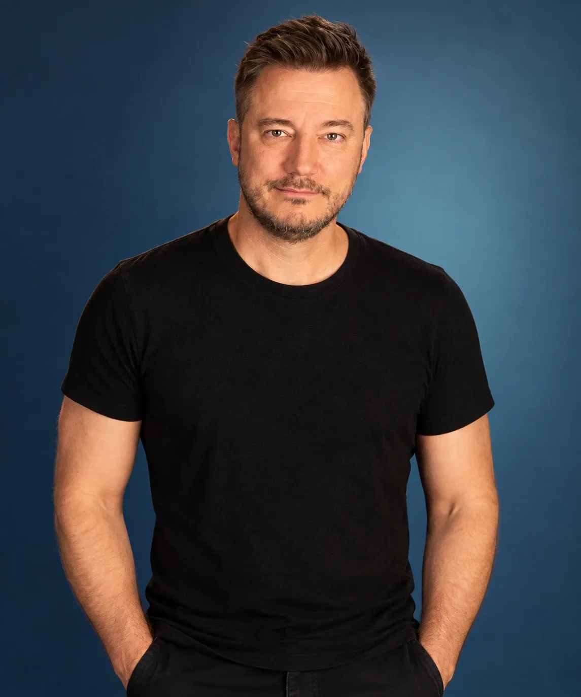 Doug Fahl in a black t-shirt, hands in his pockets, against a blue backdrop